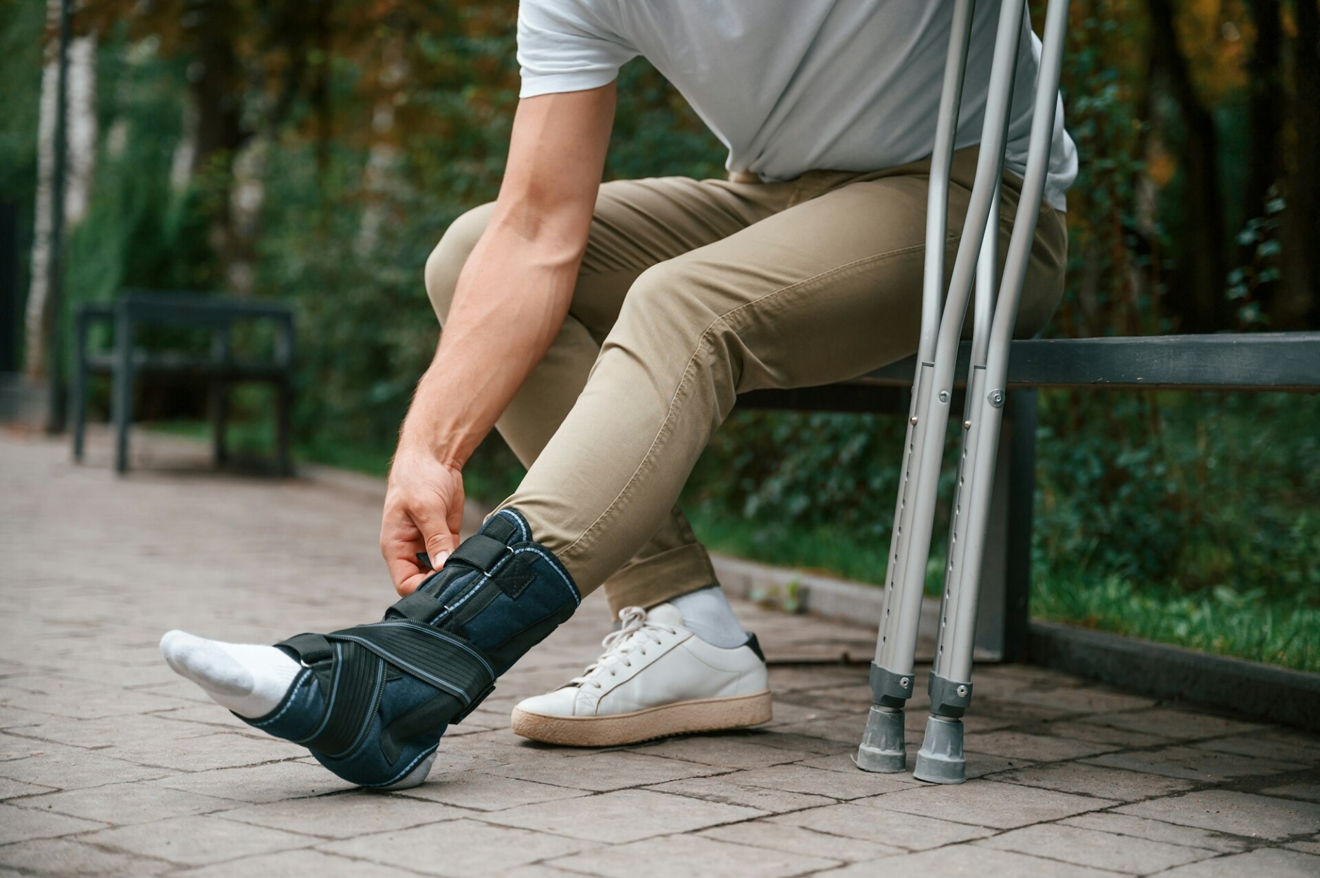 Looking at the broken leg. Man with crutches is in the park outdoors. Having leg injury